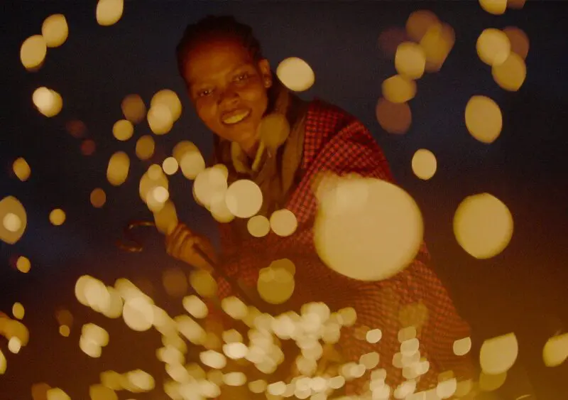 Evelyn stokes the fire, sending up a shower of glowing embers in the darkness.