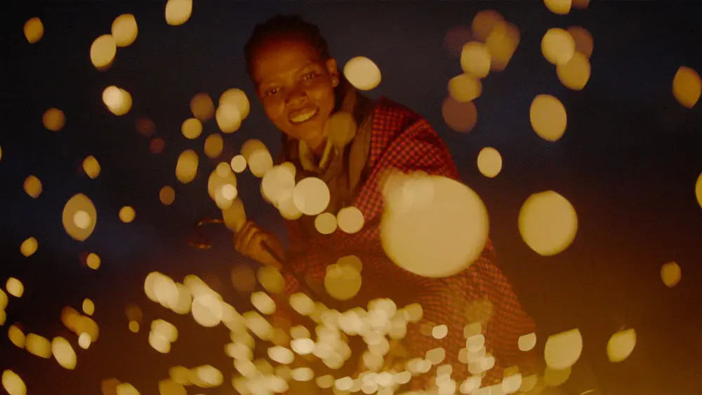 Evelyn stokes the fire, sending up a shower of glowing embers in the darkness.