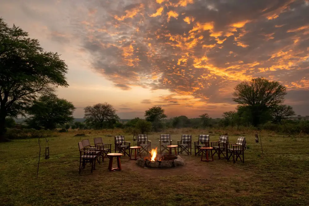 A fireside sundowner scene beneath colourful sunset skies at Sayari Camp.