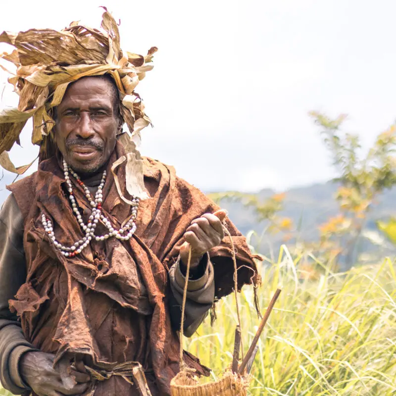 Local tribesman facing the camera with the Bwindi Impenetrable Forest behind him, Erebero Hills, Uganda