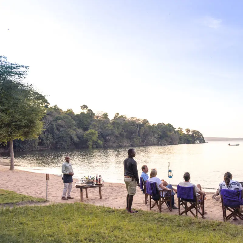 Lake Victoria, shore, guests by the fire with guide and waiter, drinks, chairs, sand
