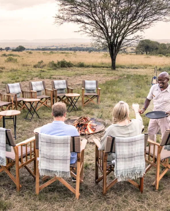 Serengeti National Park, campfire, sundowners, couple with drinks and waiter