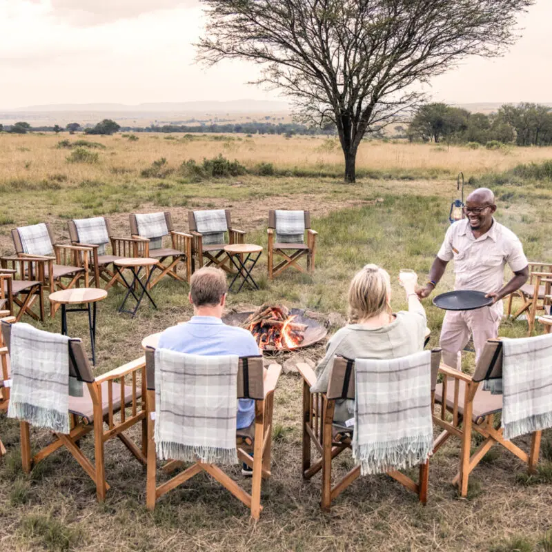 Serengeti National Park, campfire, sundowners, couple with drinks and waiter