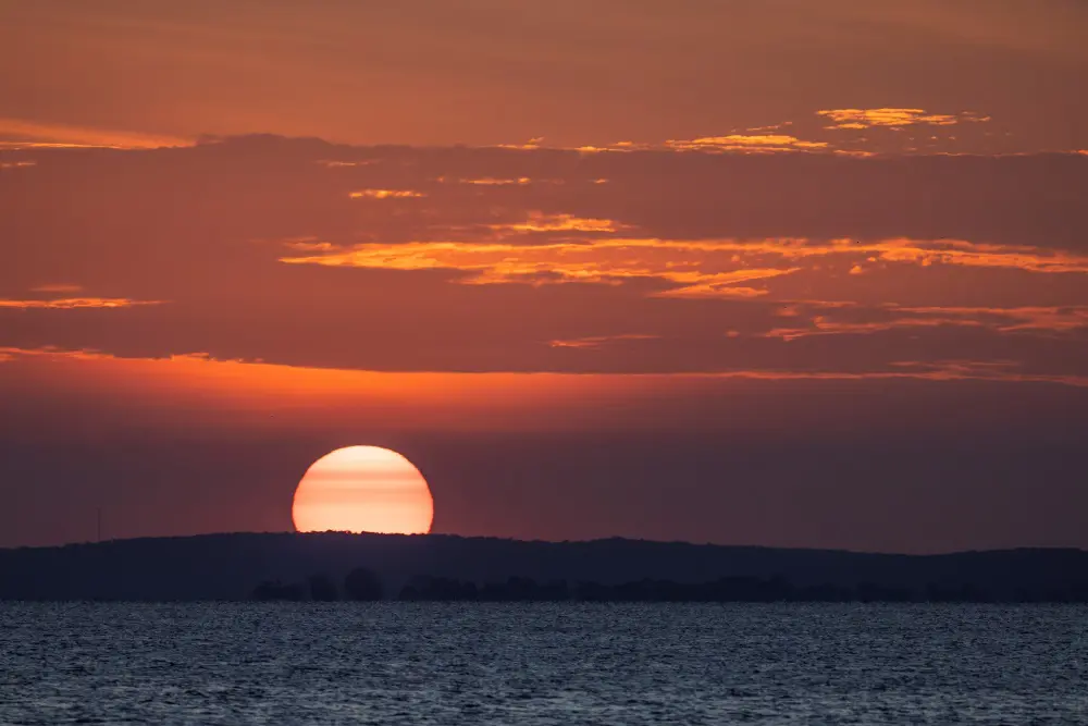 The sun breaches the horizon, turning the sky orange.