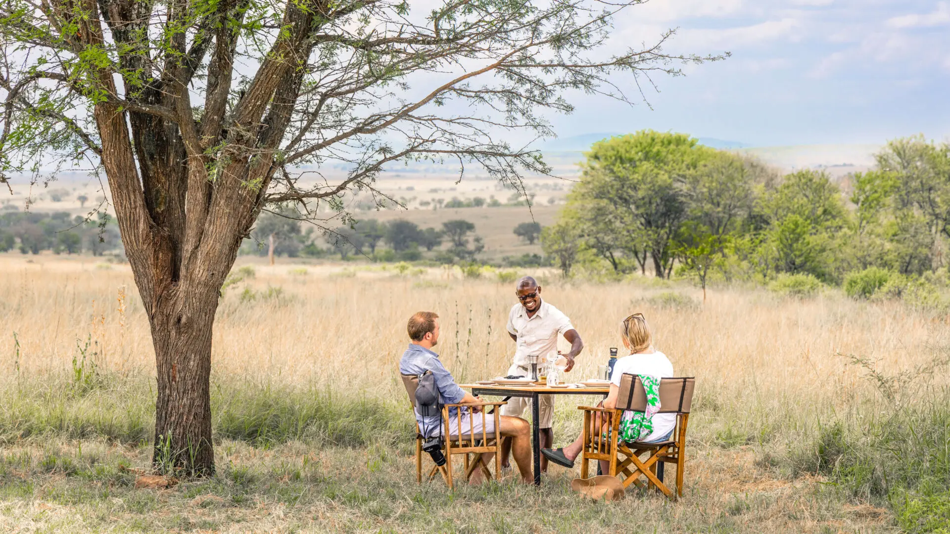 Guests and guide sitting under a tree in Serengeti National Park, guide is serving them
