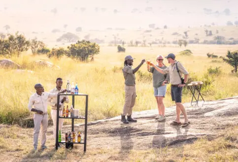 Guests enjoying a refreshing beverage on a rock with their safari guide in Serengeti National Park Tanzania
