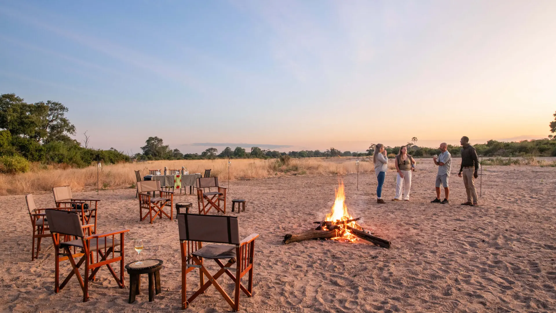 Guests around the fire while the sun sets, chairs around the campfire