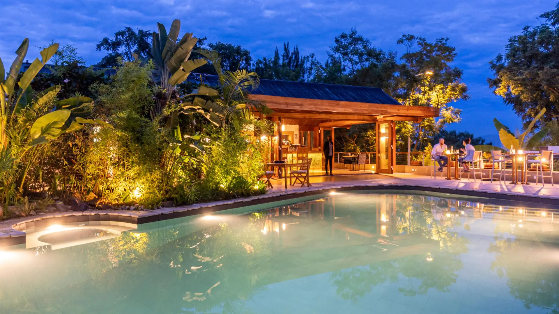 The Retreat - by pool area lit up at night with guests sitting on high tables and bar stools