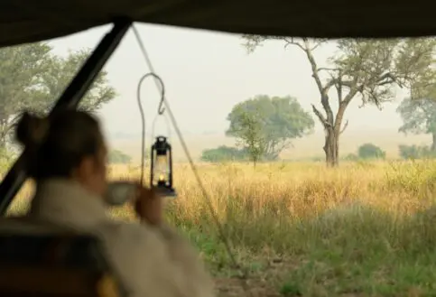 A guest enjoys a morning coffee with views across the Serengeti plains, Tanzania