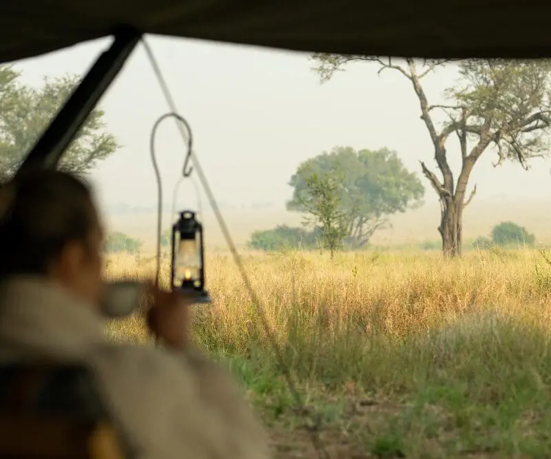 A guest enjoys a morning coffee with views across the Serengeti plains, Tanzania