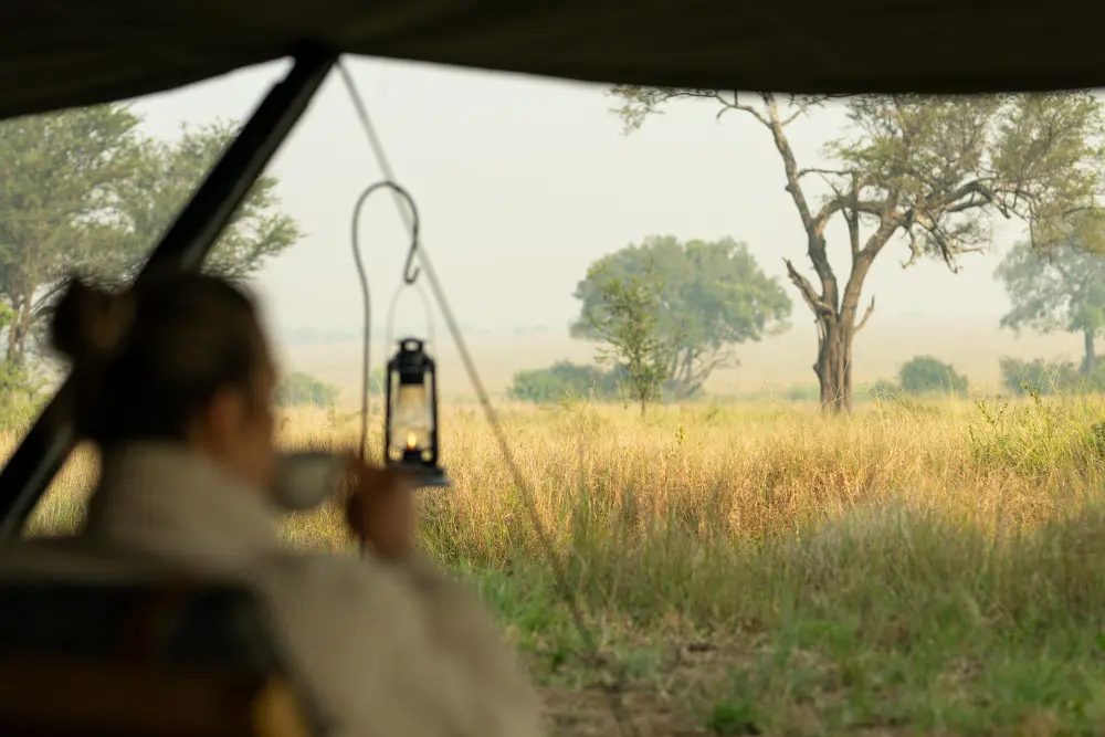 A guest enjoys a morning coffee with views across the Serengeti plains, Tanzania