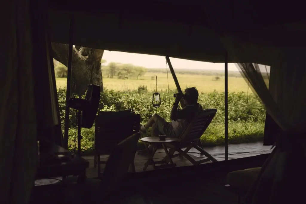 A guest sits in his tent and looks out over the wilderness using binoculars