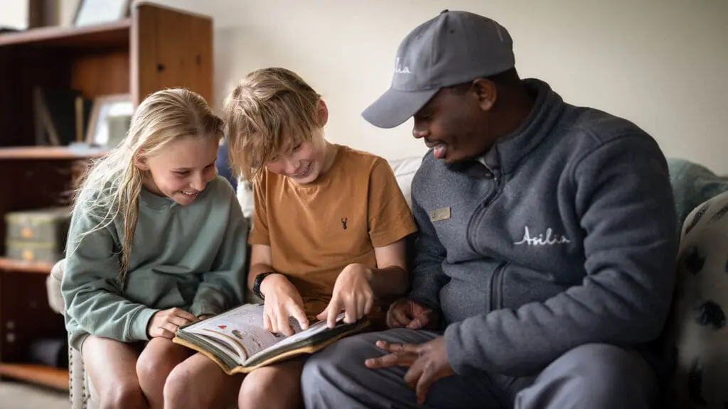 Asilia guide sitting with children in the main area reading a book and smiling