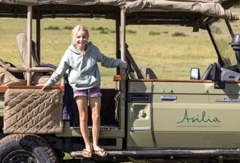 Young girl standing on the Asilia vehicle wearing shorts, flip flops and a hoodie