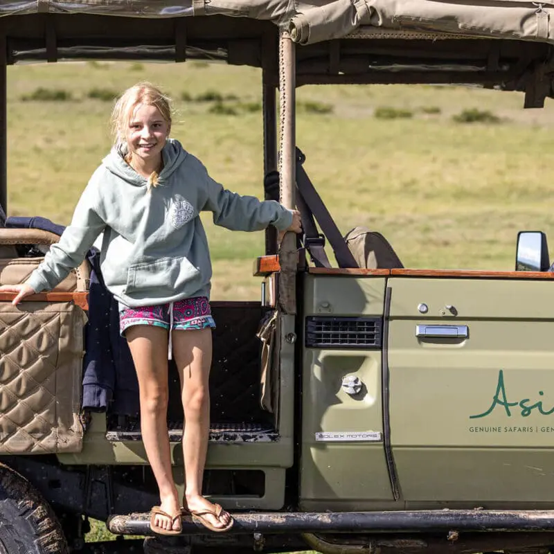 Young girl standing on the Asilia vehicle wearing shorts, flip flops and a hoodie