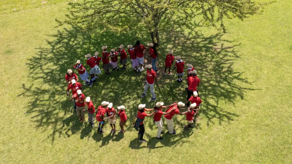 group of Twende Porini students forming a circle under the tree, singing and dancing together