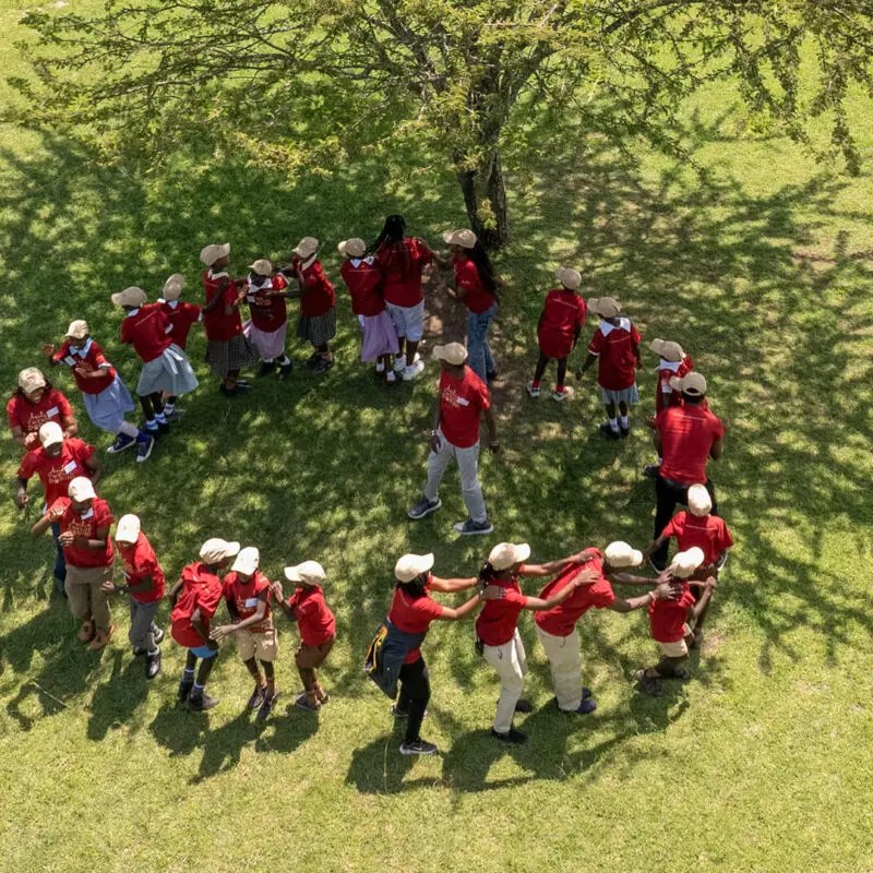 group of Twende Porini students forming a circle under the tree, singing and dancing together