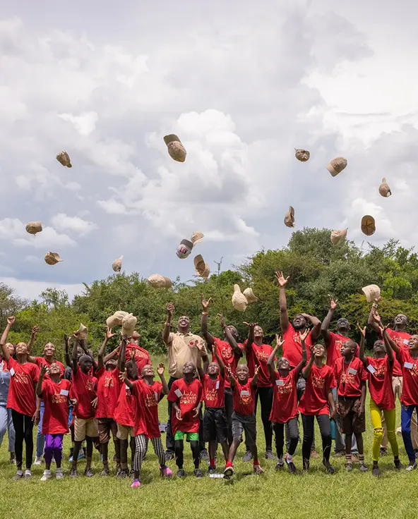 A happy group of Twende Porini students in red t-shirts throwing their caps into the air in celebration