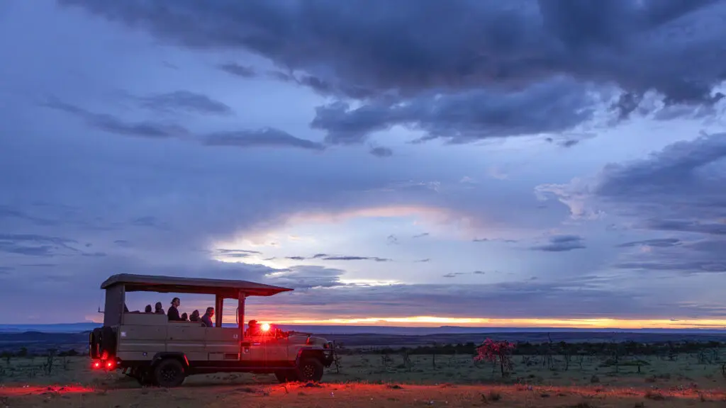 Safari vehicle parked on twilight plains, red lights glowing as passengers prepare for a night game drive