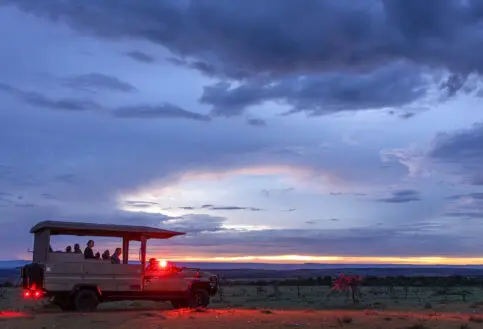 Safari vehicle parked on twilight plains, red lights glowing as passengers prepare for a night game drive