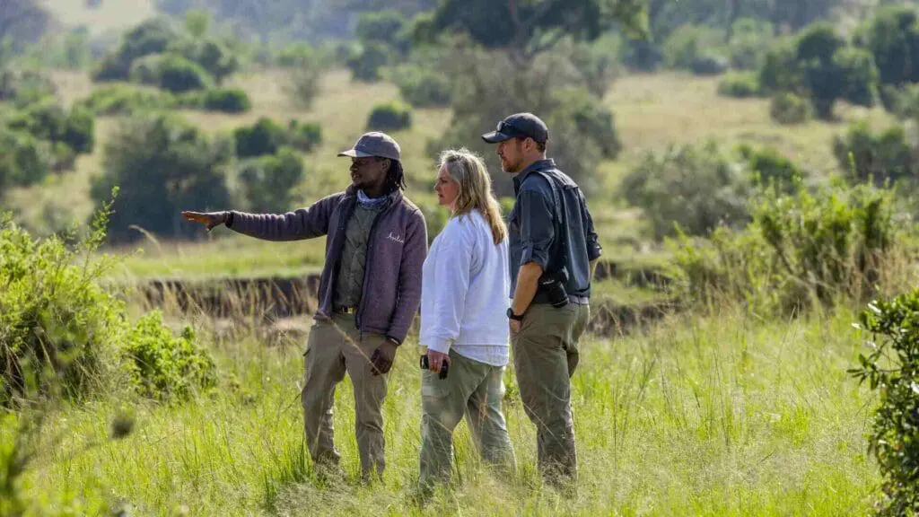 An Asilia guide points to something in the lush vegetation nearby and shares with a couple some fascinating insights