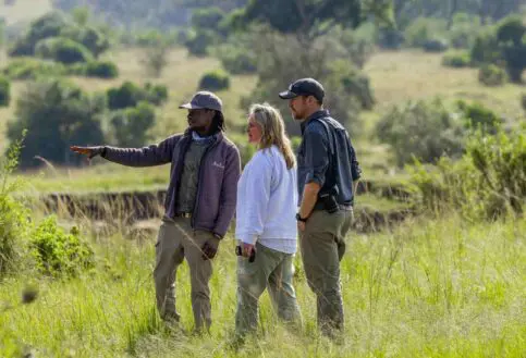 An Asilia guide points to something in the lush vegetation nearby and shares with a couple some fascinating insights