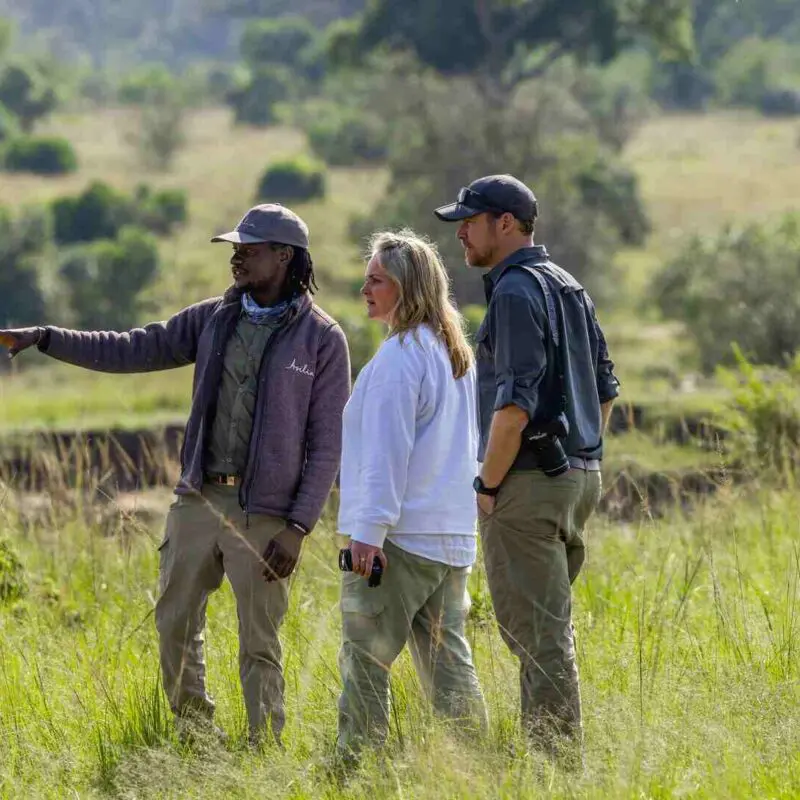 An Asilia guide points to something in the lush vegetation nearby and shares with a couple some fascinating insights