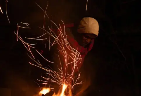 An Askari stokes the fire sending embers fling through the dark night