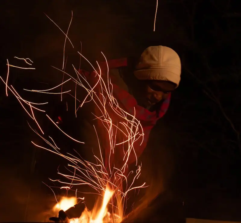 An Askari stokes the fire sending embers fling through the dark night