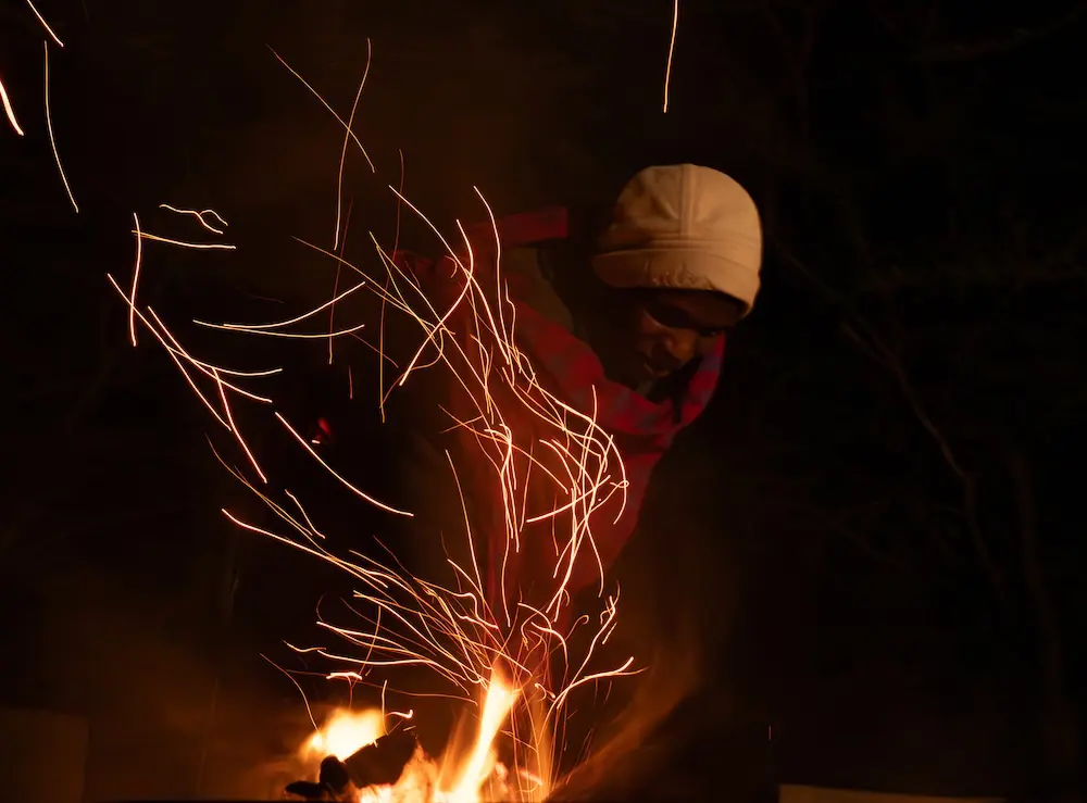 An Askari stokes the fire sending embers fling through the dark night