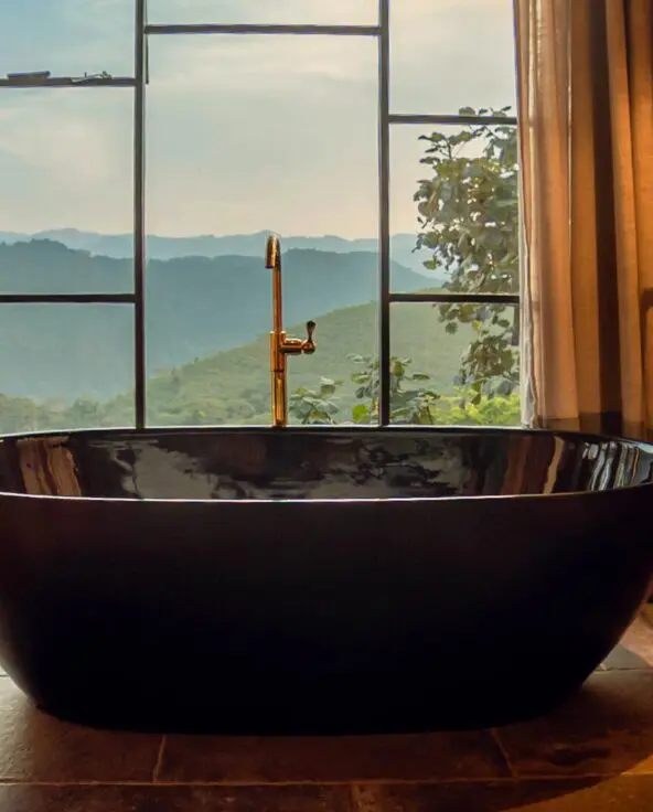 Freestanding black bathtub beside floor-to-ceiling windows overlooking the forested hills at Erebero Hills.