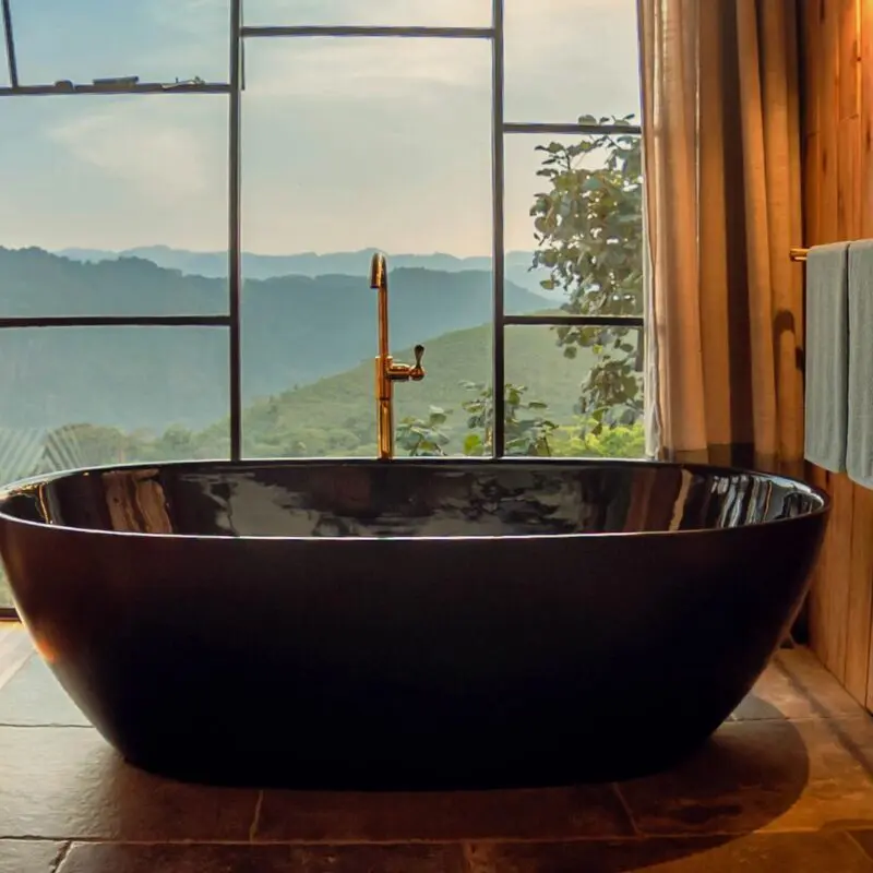Freestanding black bathtub beside floor-to-ceiling windows overlooking the forested hills at Erebero Hills.