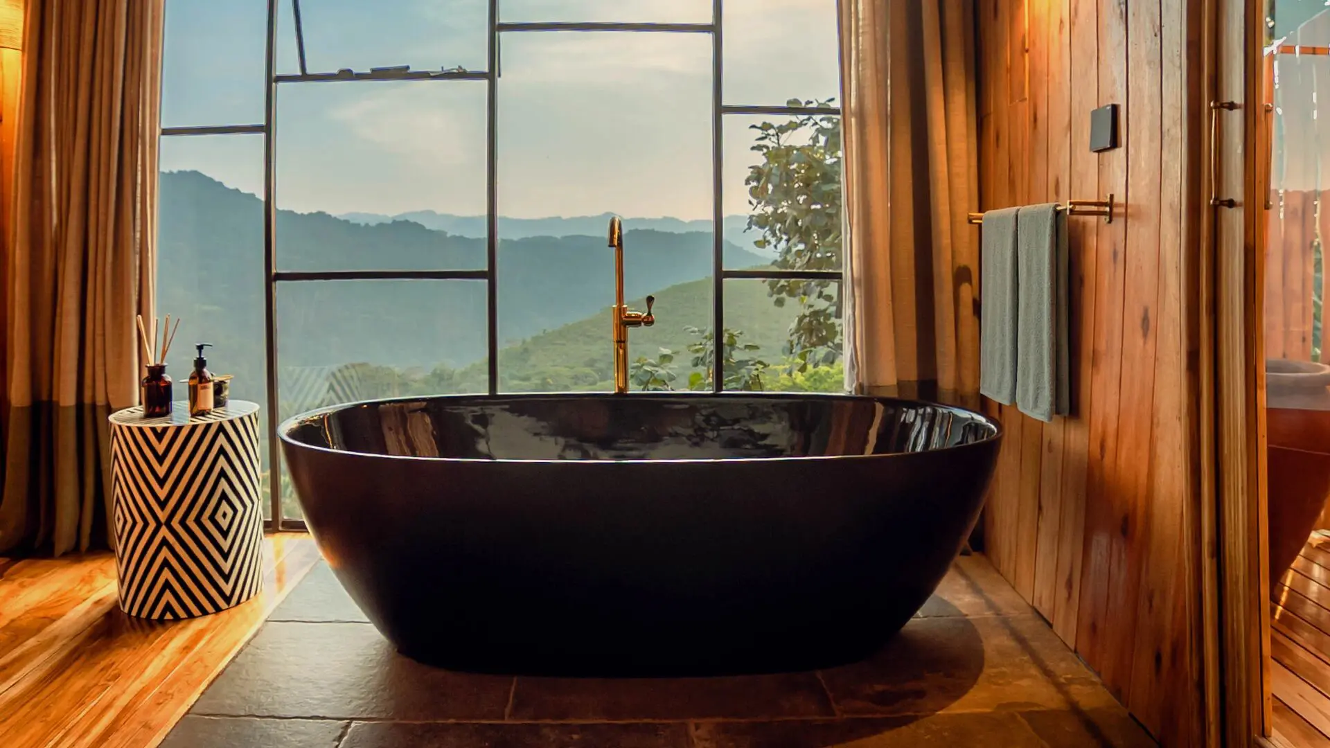 Freestanding black bathtub beside floor-to-ceiling windows overlooking the forested hills at Erebero Hills.