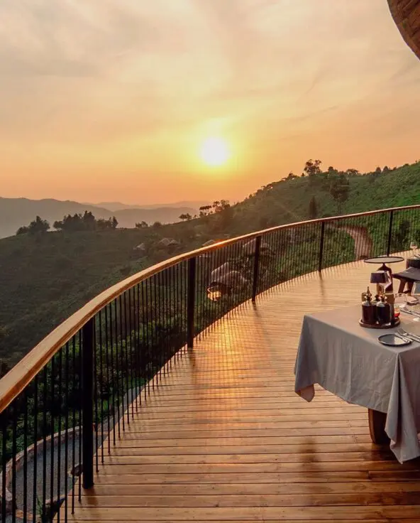 Outdoor dining table on the curved wooden terrace at Erebero Hills overlooking forested hills at sunset.