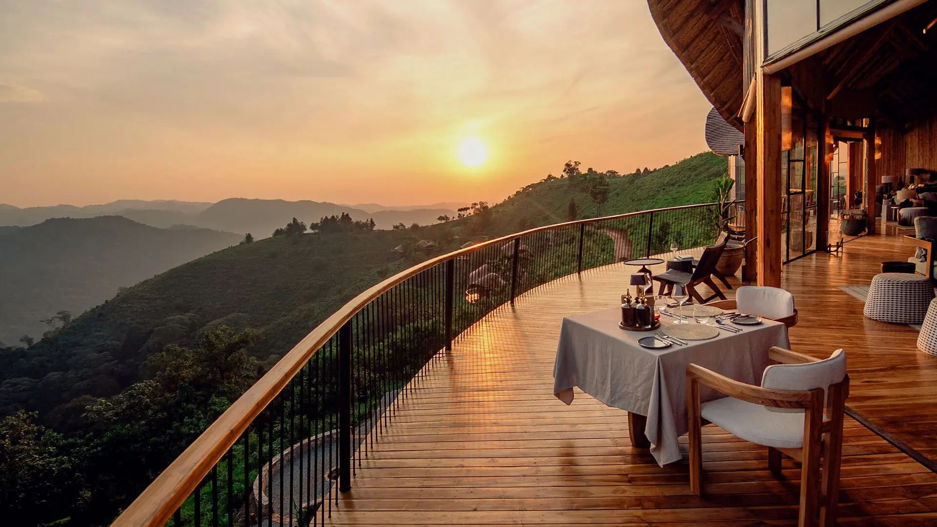 Outdoor dining table on the curved wooden terrace at Erebero Hills overlooking forested hills at sunset.