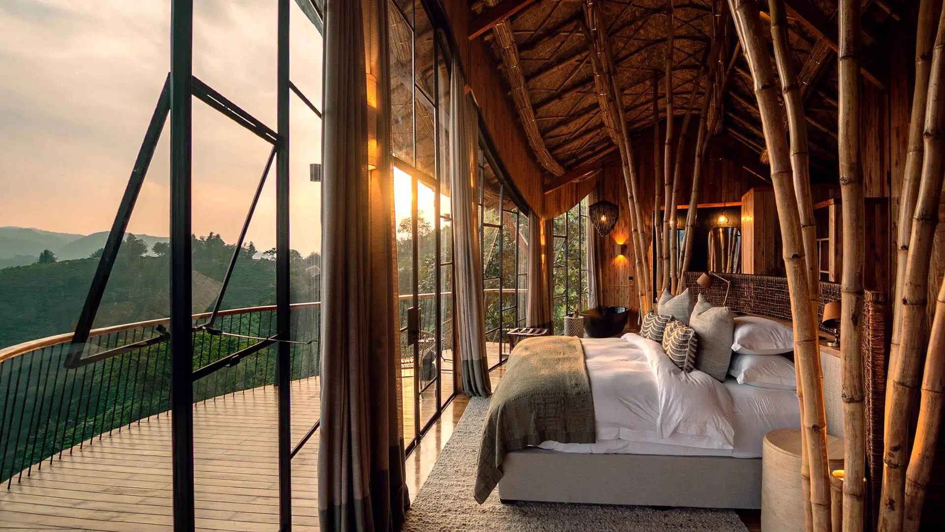 Warmly lit lodge bedroom at Erebero Hills, with a large bed, bamboo detailing and floor-to-ceiling windows opening onto a balcony and forested hills.