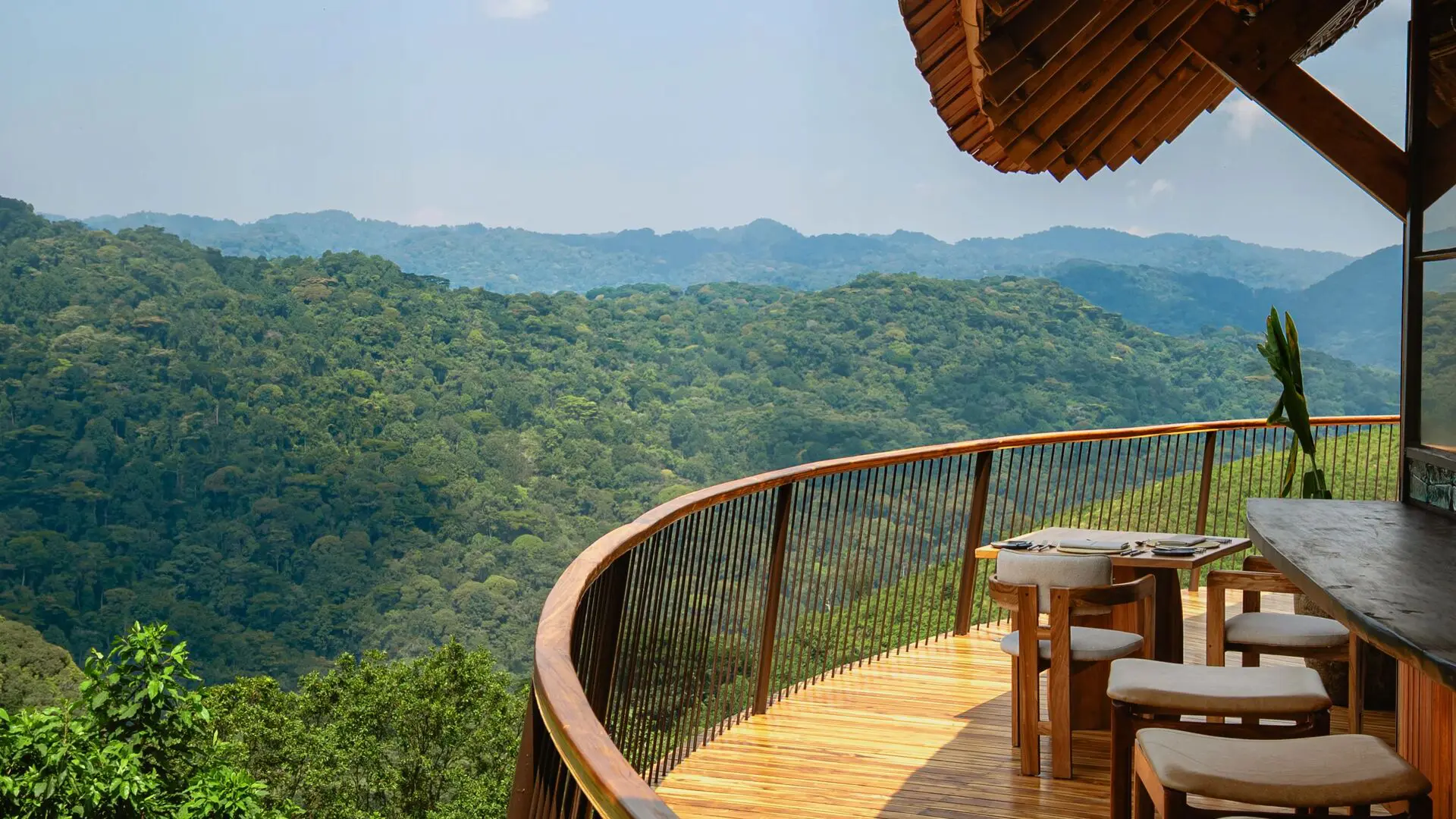 The curved wooden deck of Erebero Hills with a dining table and chairs overlooking the expansive, densely forested hills of Bwindi