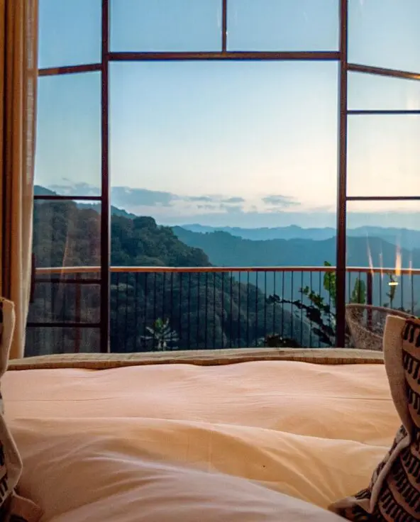 Views from your lodge bed through tall glass doors toward your private deck and layers of forested mountains in the distance.