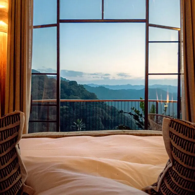 Views from your lodge bed through tall glass doors toward your private deck and layers of forested mountains in the distance.
