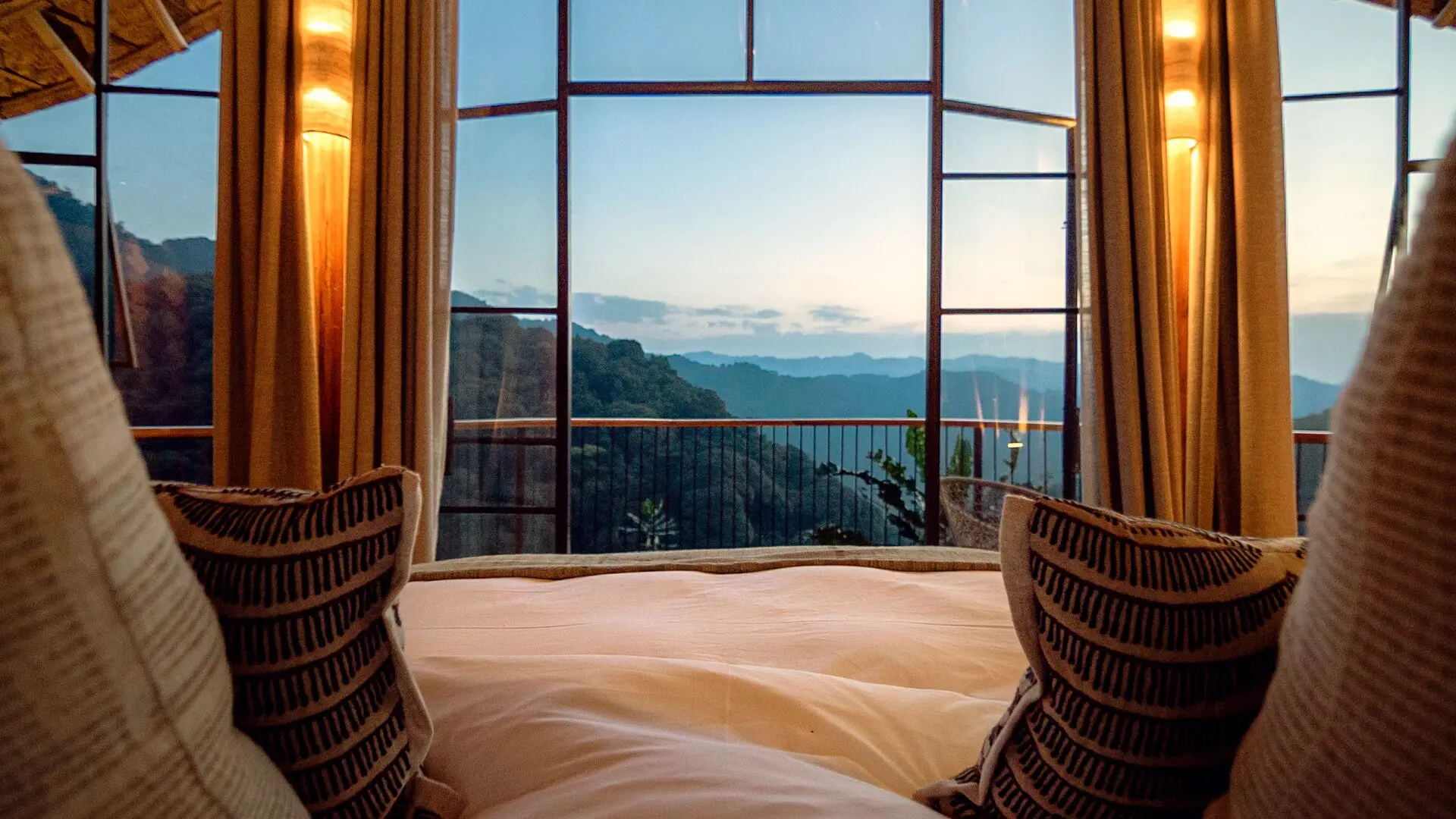 Views from your lodge bed through tall glass doors toward your private deck and layers of forested mountains in the distance.