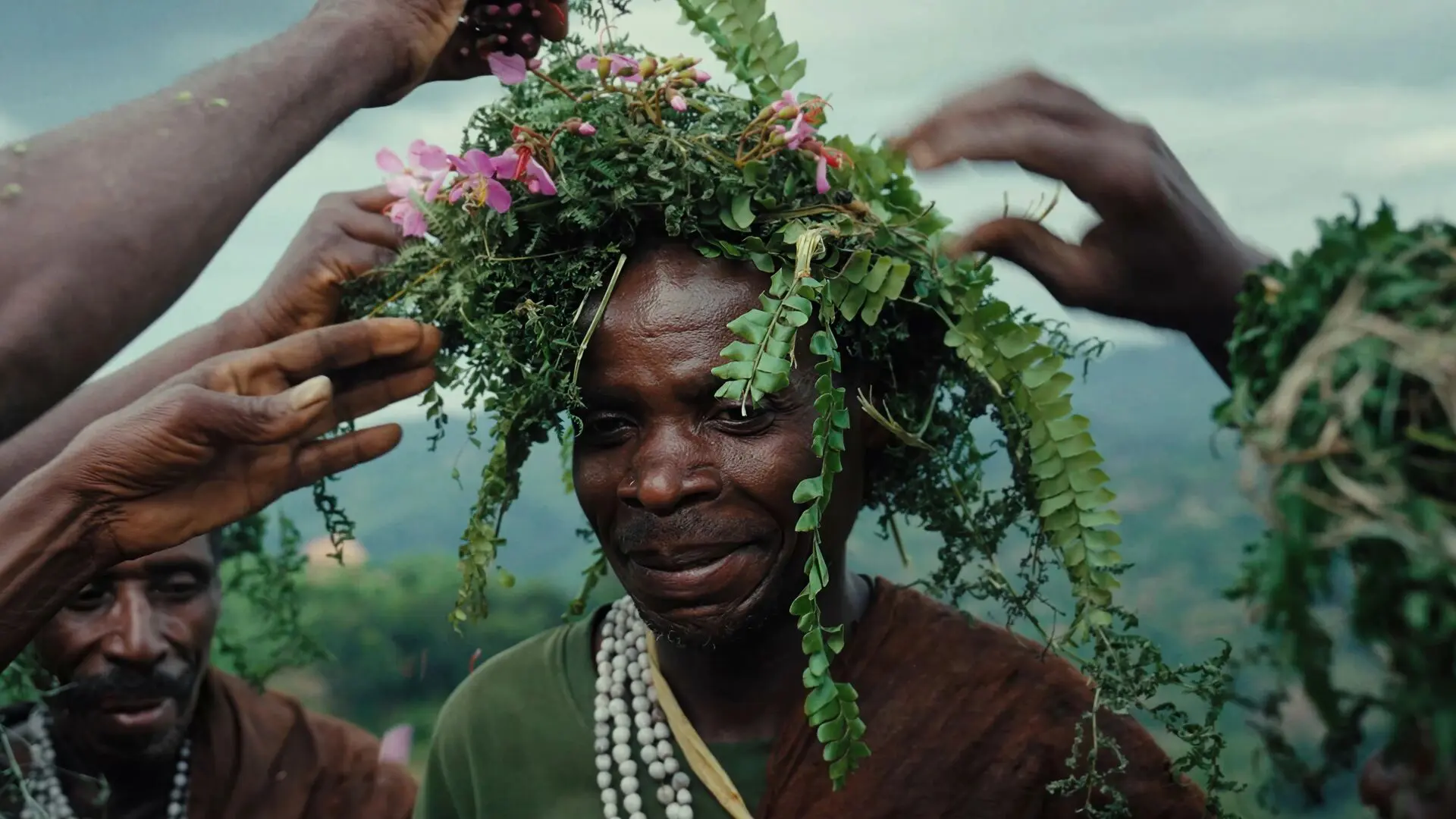 Hands of the Batwa placing flowers on a mans head during a ceremony in Bwindi