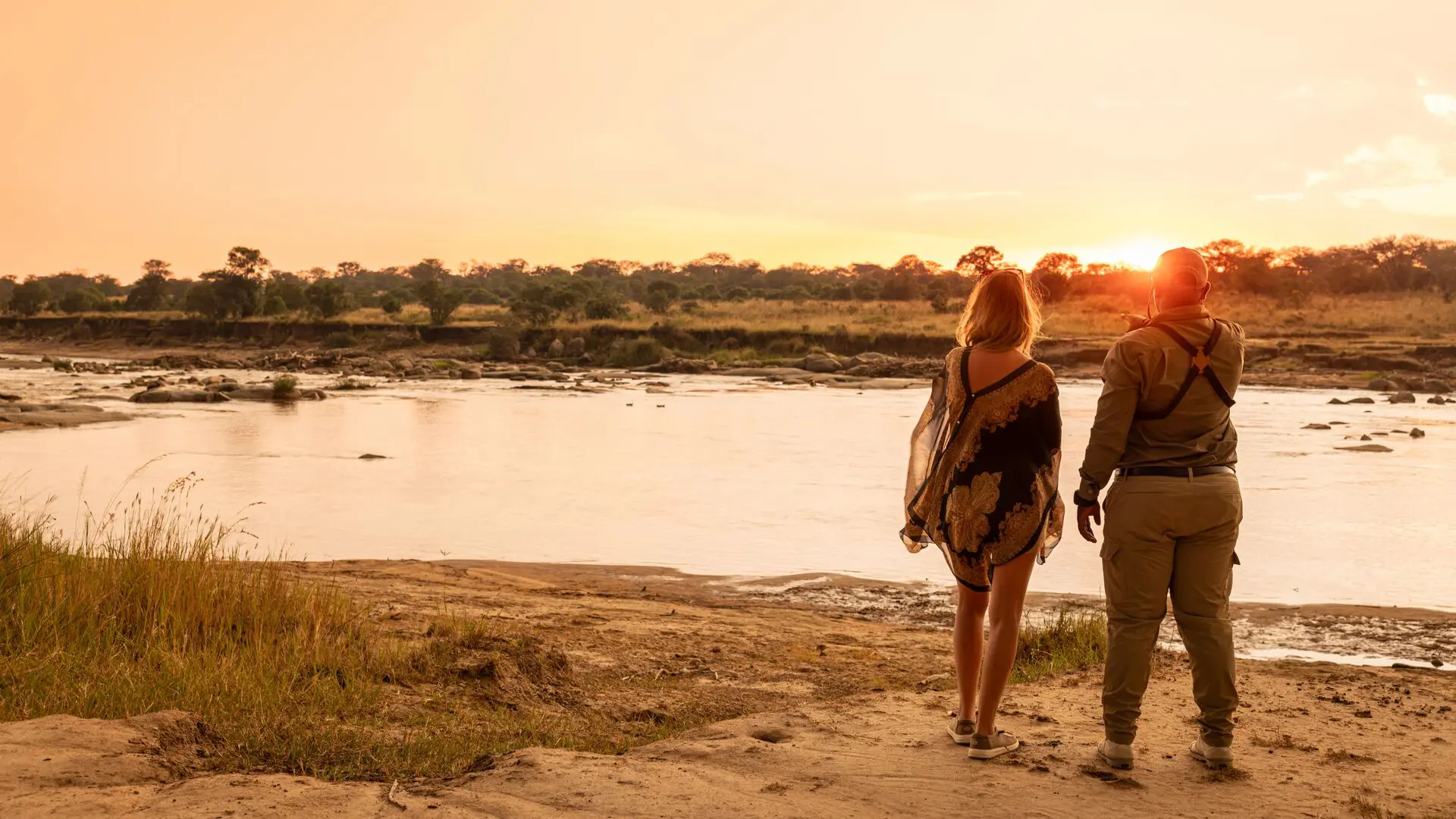 Guest and safari guide standing beside a river at sunset near Olakira Camp in Tanzania