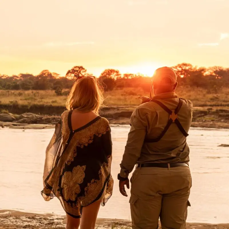 Guest and safari guide standing beside a river at sunset near Olakira Camp in Tanzania
