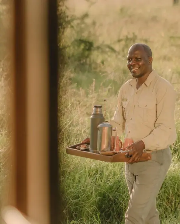 Asilia staff member carrying a tray with coffee through the grass at Naboisho Camp, Kenya.