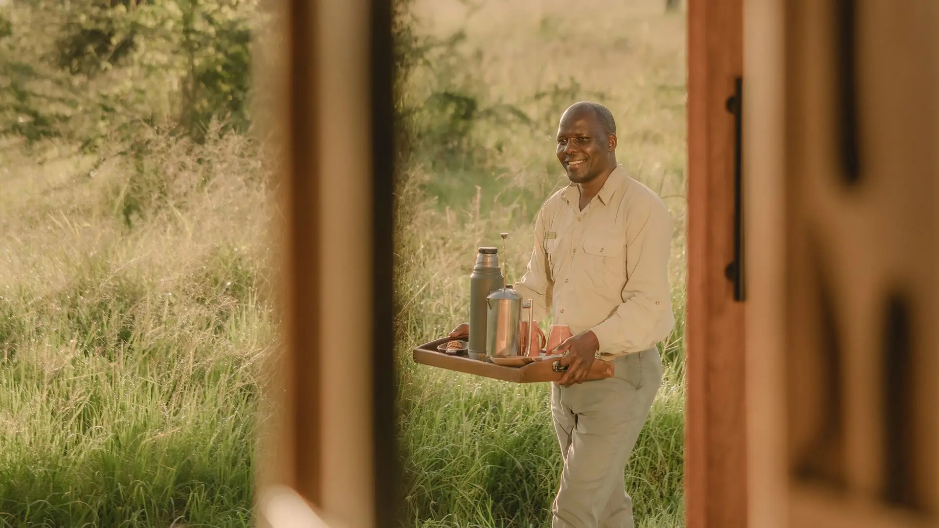 Asilia staff member carrying a tray with coffee through the grass at Naboisho Camp, Kenya.