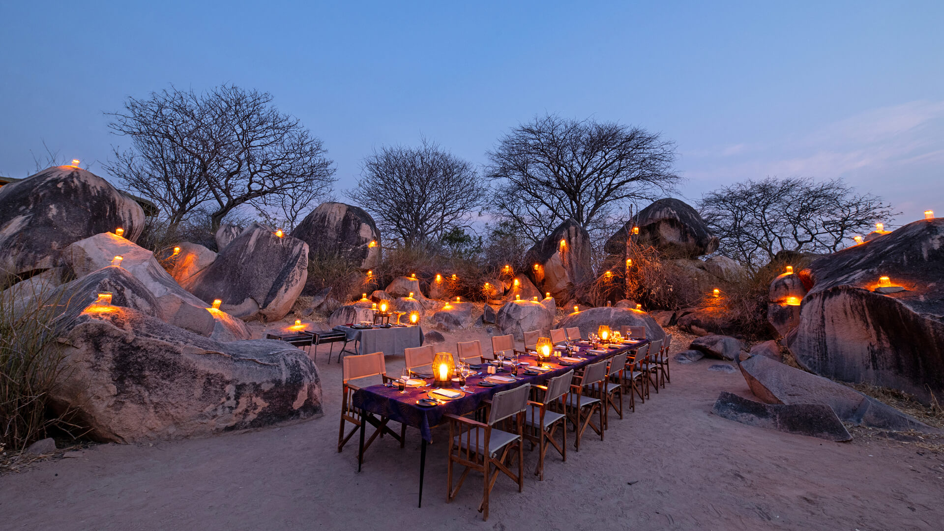 A luxurious dinner set up in the outdoors, surrounded by boulders
