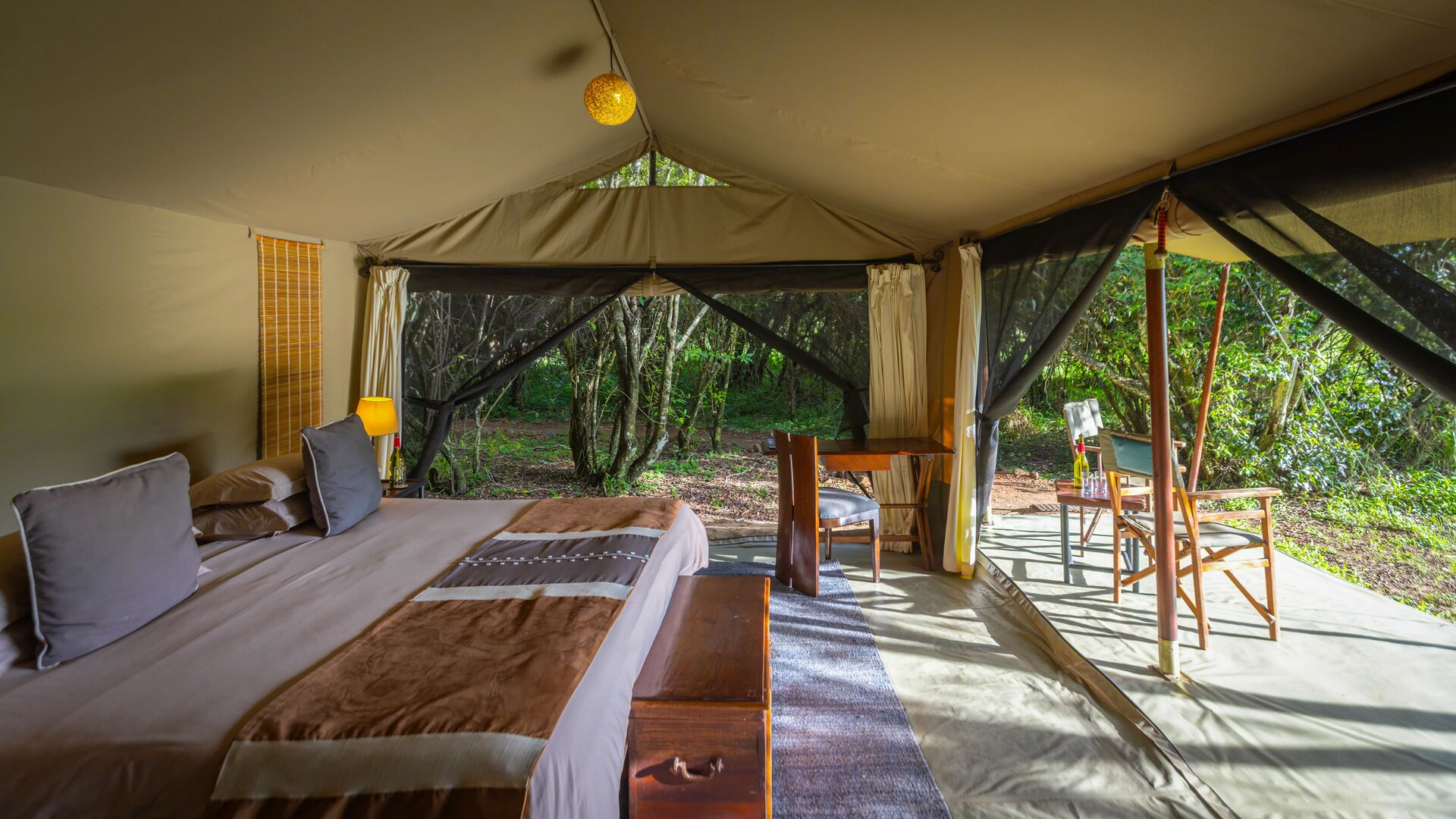 A safari tent bedroom with large bed, bedside tables, and soft ambient lighting