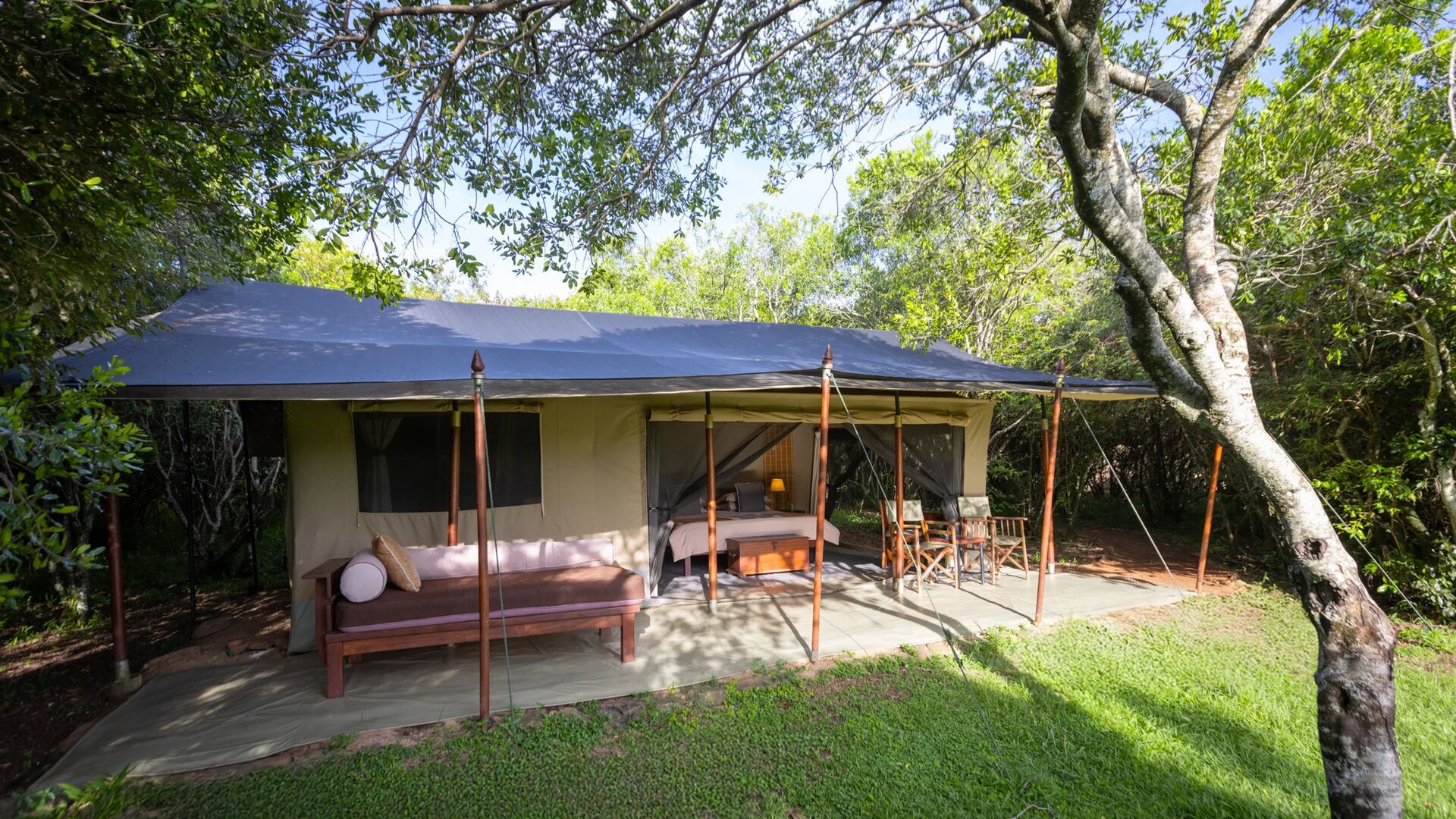 Spacious luxury safari tent with veranda, seating, and bed, surrounded by trees and greenery - encounter mara camp - asilia africa
