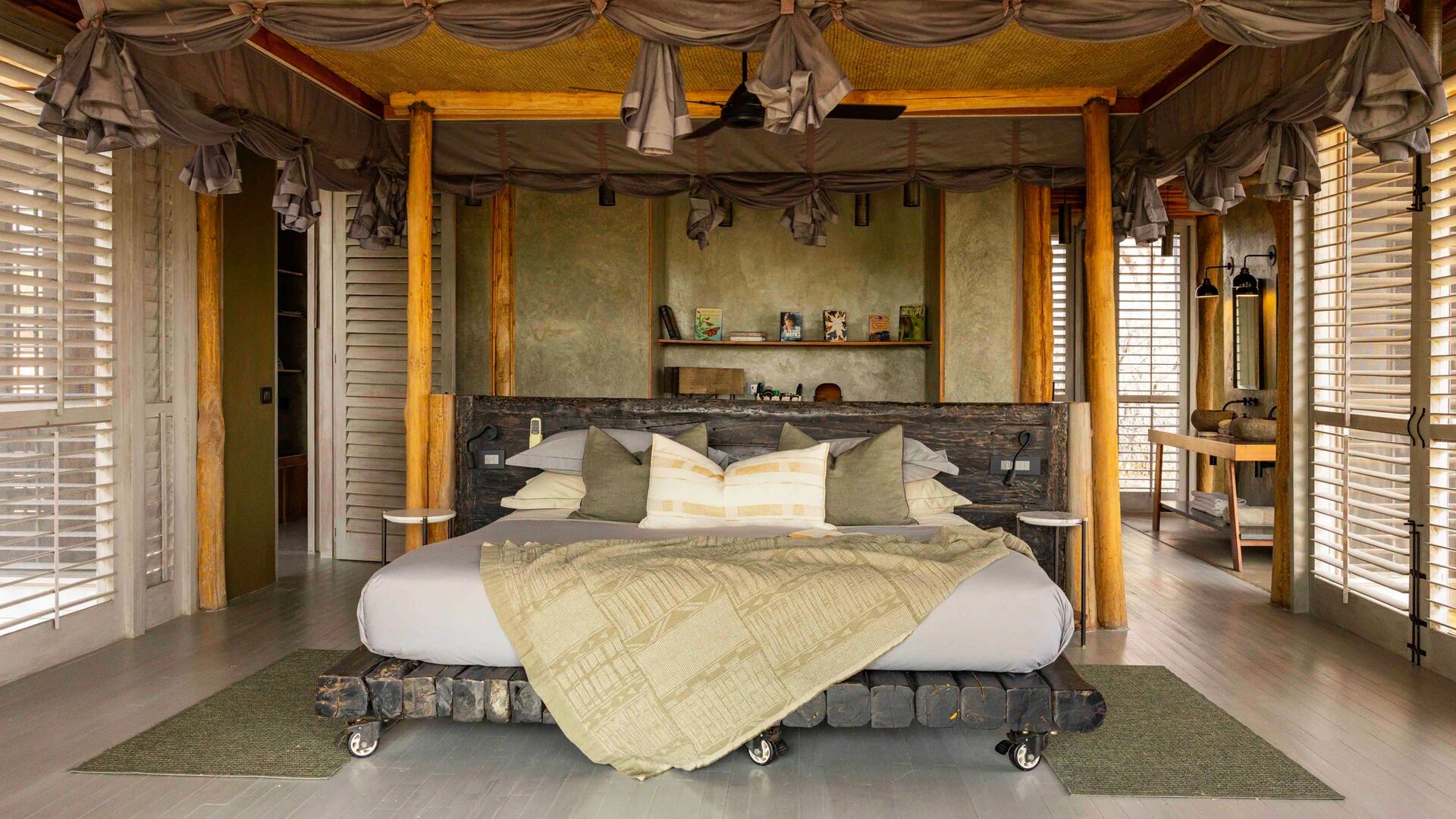 Jabali Private House - spacious safari lodge double bedroom with a four-poster bed draped in soft linens, wooden pillars, open shutters, and natural light flowing through the room.