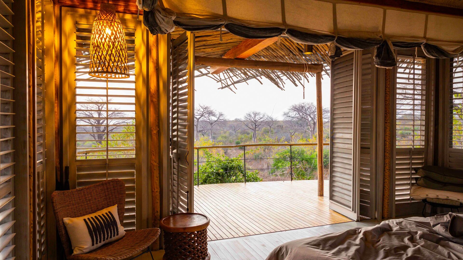 interior of a suite at jabali camp with open wooden shutters leading onto a private deck, overlooking trees and open woodland, with soft natural light and woven furnishings inside